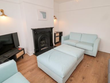 A living room with two light blue sofas a large ottoman a black fireplace a TV on a dark wooden stand and wooden flooring at Shileen in Seahouses
