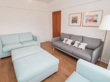 A living room with a grey sofa with cushions a light blue armchair and ottoman wooden floor and framed pictures on the wall at Shileen in Seahouses