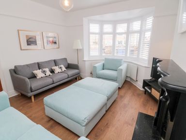 A living room with a grey sofa two blue armchairs ottoman a floor lamp and television at Shileen in Seahouses