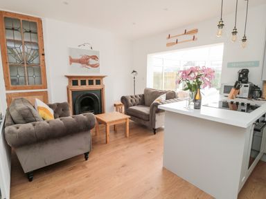 A living room with two sofas a coffee table and fireplace next to a kitchen island with flowers and wine at Shileen in Seahouses