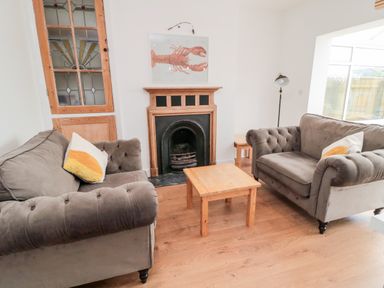 A living room with two gray sofas a wooden coffee table a fireplace and a stained glass cabinet at Shileen in Seahouses