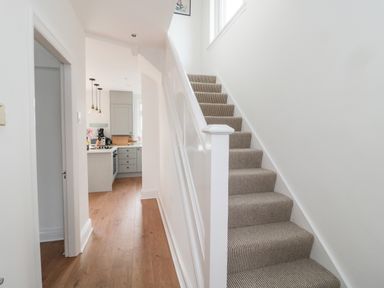 A hallway with wooden floor leading to a kitchen and carpeted stairs on the right at Shileen in Seahouses