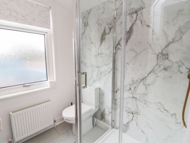 A bathroom with a toilet next to a glass shower enclosure and a frosted window at Shileen in Seahouses
