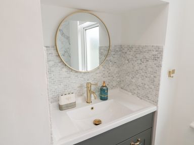 A bathroom sink with a gold faucet a round mirror and tiled backsplash at Shileen in Seahouses