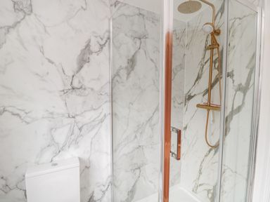 A bathroom with a toilet and a glass shower enclosure with a gold showerhead at Shileen in Seahouses