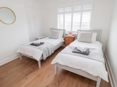 A bedroom with two single beds bedside table and window shutters at Shileen in Seahouses