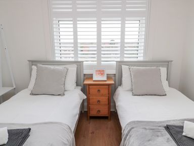 A bedroom with two single beds a wooden nightstand between them and window shutters at Shileen in Seahouses