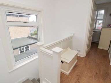 A hallway with wooden flooring a white wooden bench a window overlooking a roof and an open door leading to a room at Shileen in Seahouses