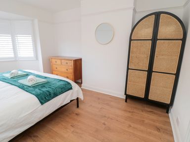 A bedroom with a bed, wooden dresser, arched wardrobe, round mirror, and window with shutters at Shileen in Seahouses