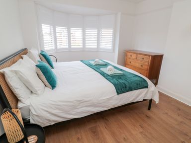 A bedroom with a bed with white bedding and teal accents next to a wooden dresser at Shileen in Seahouses