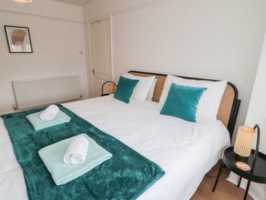 A bedroom with a double bed with teal pillows and blankets and rolled white towels at Shileen in Seahouses