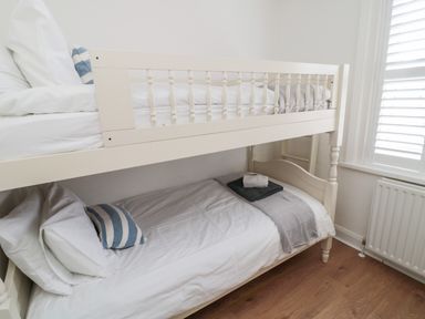 A bunk bed with white bedding and pillows in a room with wooden floor and a window with white shutters at Shileen in Seahouses