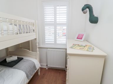 A small bedroom with a bunk bed a window with shutters a chest of drawers with books and a framed picture and a dinosaur wall decoration at Shileen in Seahouses