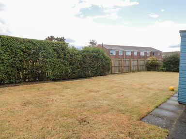 A backyard with trimmed hedges and a wooden fence next to a paved walkway at Shileen in Seahouses