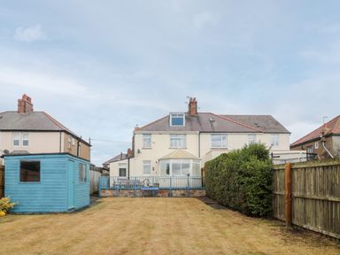 A backyard garden with a blue shed a lawn and a two story house at Shileen in Seahouses