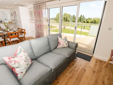 A living room with grey sofa and floral cushions next to a dining table with wooden chairs and a kitchen area at Amarone in Seaview