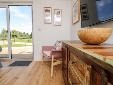 A wooden cabinet with a bowl on it a pink chair with cushions framed pictures on a white wall and glass doors opening to a garden at Amarone Seaview