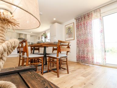 A dining area with a wooden table and chairs near a kitchen and a window with patterned curtains at Amarone in Seaview