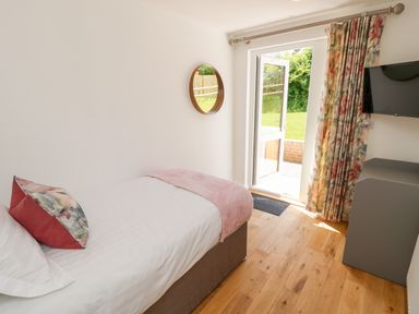 A bedroom with a single bed a pillow, blanket, round mirror on the wall, open door leading outside, floral curtains, wall-mounted television, and wooden floor at Amarone in Seaview
