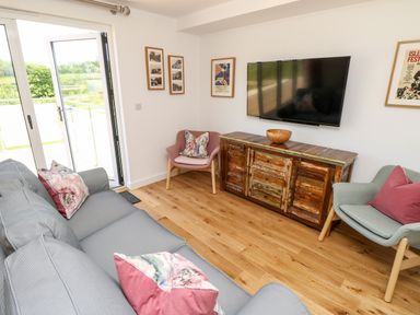 A living room with a gray sofa and floral cushions two armchairs a wooden TV stand with a bowl and a wall-mounted TV at Champagne Seaview