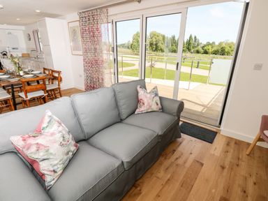 A living room with a gray sofa and floral pillows next to sliding glass doors opening to a deck and a view of a green lawn at Champagne in Seaview