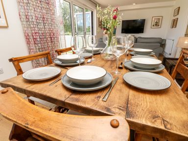 A dining table set with plates bowls wine glasses and cutlery in a room with wooden chairs and a television on the wall at Champagne in Seaview