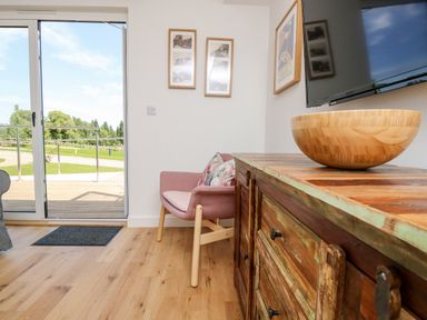 A room with a wooden cabinet holding a wooden bowl a pink armchair and sliding glass doors leading outside at Champagne in Seaview