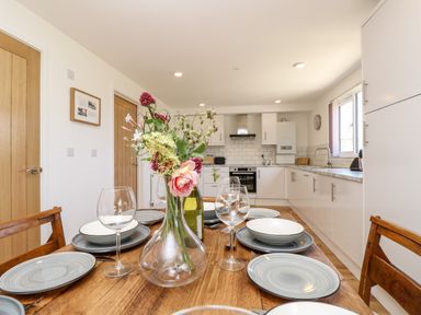 A dining table set with plates and glasses with a vase of flowers in a kitchen with white cabinets at Champagne in Seaview