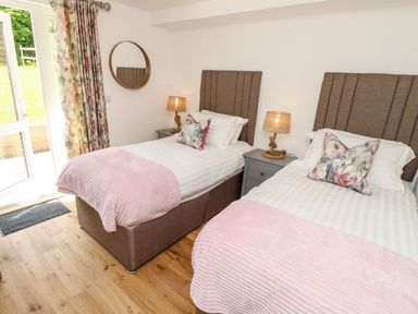 A bedroom with two single beds pink throws floral cushions round wall mirror and bedside tables with lamps at Champagne in Seaview