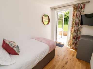 A bedroom with a single bed pillows blanket a round mirror a television and a door open to a garden at Champagne Seaview