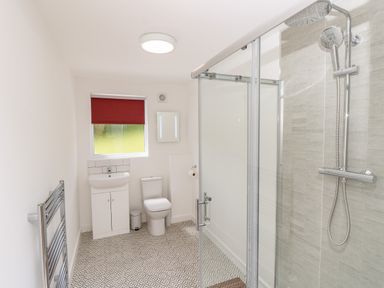 A bathroom with a shower enclosure a toilet a sink with cabinet a red window blind and a heated towel rail at Champagne in Seaview
