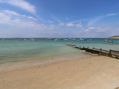 A beach with sand and a wooden pier extending into the sea with boats on the water at Barolo in Seaview