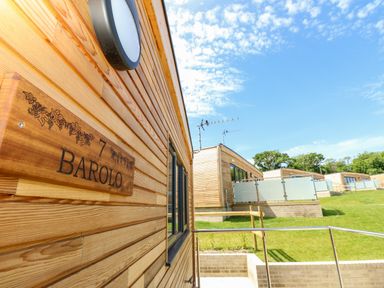 A wooden exterior wall with a Barolo sign and neighbouring wooden lodges on a grassy slope at Barolo in Seaview