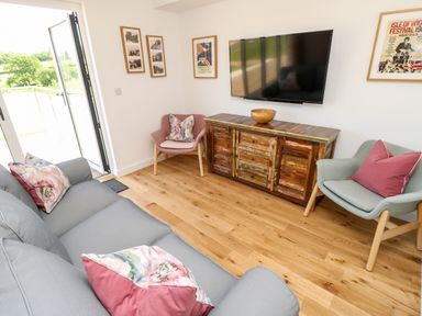 A living room with a grey sofa and floral cushions two armchairs a wooden cabinet with a bowl and a wall-mounted television at Barolo in Seaview