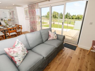 A living room with a gray sofa and floral cushions near sliding glass doors opening to a wooden deck and green lawn at Barolo in Seaview