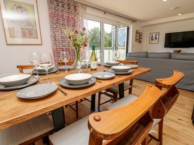 A dining table set with plates glasses and a vase of flowers next to a living area with a grey sofa and a wall mounted TV at Barolo in Seaview