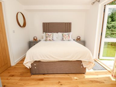 A bedroom with a bed two bedside tables and lamps a round mirror on the wall and an open door to a garden at Barolo in Seaview