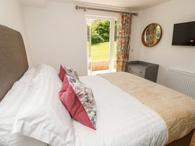 A bedroom with a bed with pillows a dresser a round mirror a wall-mounted TV and open doors to a garden at Barolo in Seaview