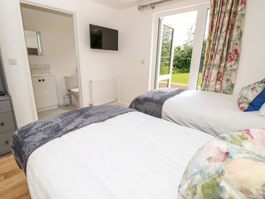 A bedroom with two single beds a wall mounted TV an open door to a bathroom and glass doors opening to a garden at Barolo in Seaview