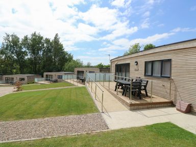 Exterior view of wooden lodges with outdoor seating and railings surrounded by grass and trees at Barolo in Seaview