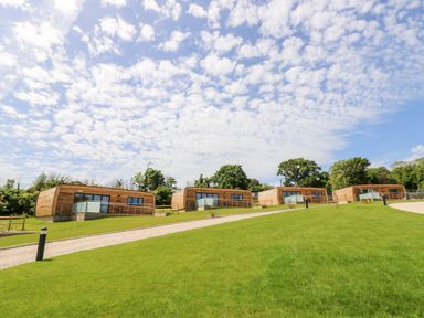 Four wooden cabins on a grassy hill with a gravel path and trees in the background at Cava Seaview