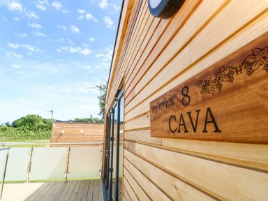 Wooden exterior wall with a plaque reading 8 Cava on a balcony with glass railing and blue sky at Cava in Seaview