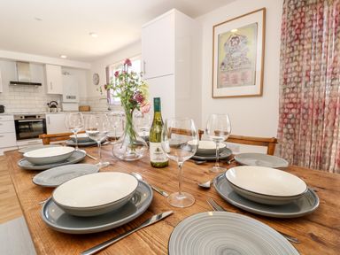 A dining table set with plates glasses a bottle of wine and flowers in a kitchen at Cava in Seaview