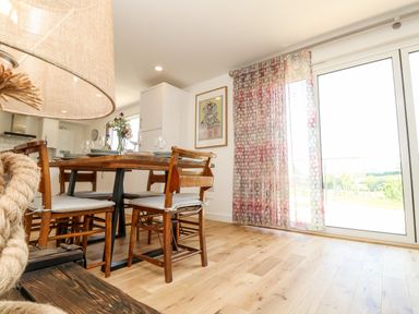 A dining area with wooden chairs and a table set with glassware and plates next to sliding glass doors with patterned curtains at Cava in Seaview