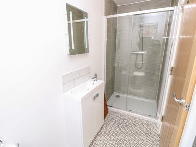 A bathroom with a glass shower enclosure a white sink cabinet a mirror and patterned floor tiles at Cava in Seaview