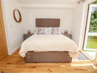 A bedroom with a bed and bedside tables with lamps and an open door showing a garden at Cava in Seaview