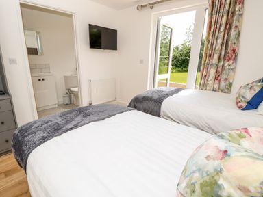 A bedroom with two beds a wall mounted tv an open door to a bathroom and glass doors opening to a garden at Cava in Seaview