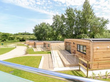 A row of wooden lodges with ramps and pathways surrounded by grass and trees at Cava in Seaview