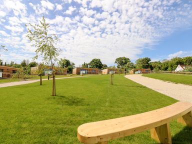 Green lawn with small trees wooden bench and modern wooden buildings under blue sky at Cava in Seaview