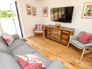 A living room with a gray sofa and pink and floral cushions a wooden cabinet with a bowl and a wall-mounted TV two chairs with cushions and framed pictures on the wall at Chianti in Seaview